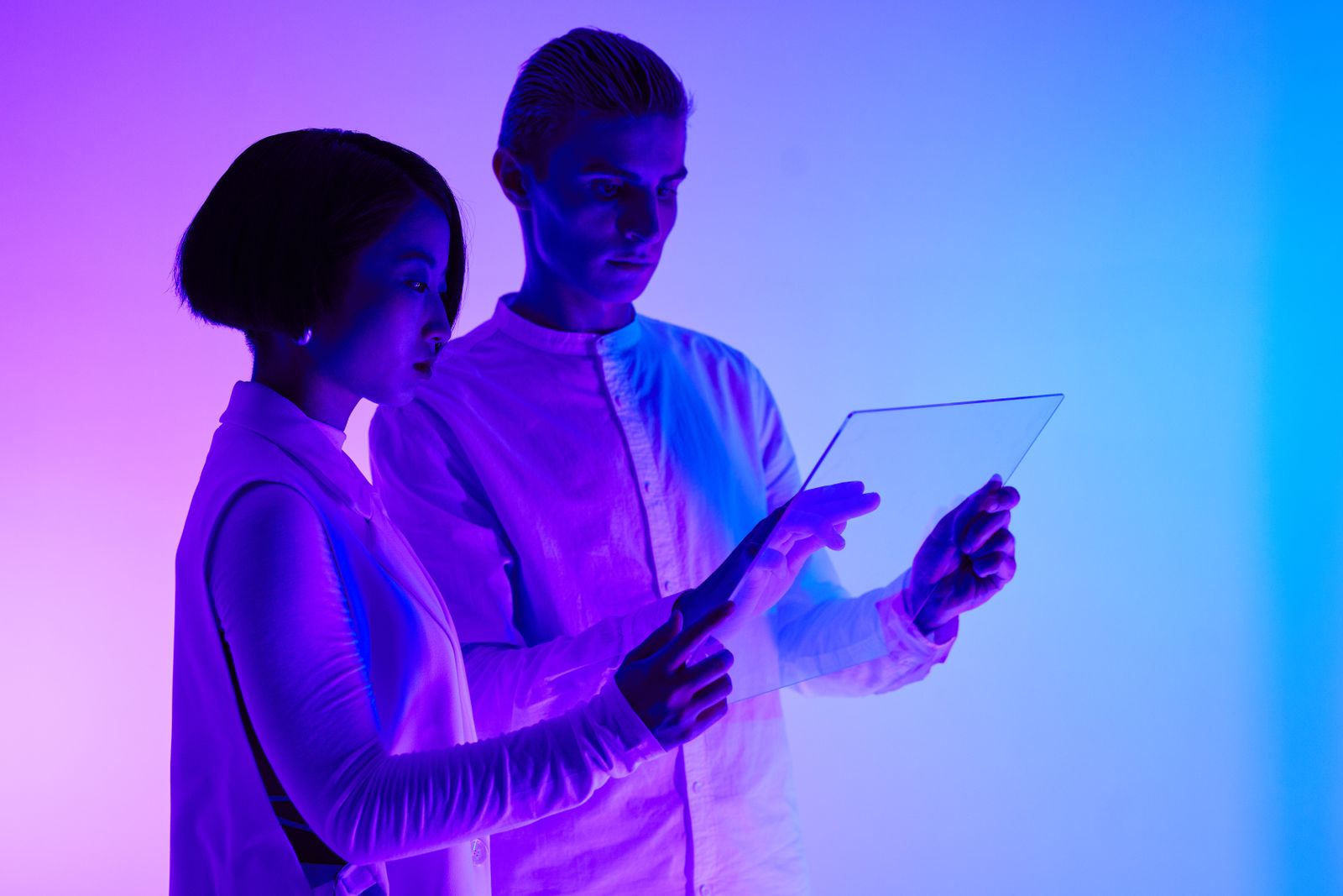 Homem e mulher interagindo com tela transparente iluminada por luzes roxas e azuis